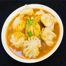 A plate of dumplings drizzled with sauce, showcasing the culinary delights of Indian and Nepali cuisine.